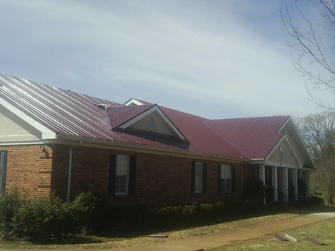 Red metal roof with gabled entries on a long brick building, from a Hail Damage Roof Repair job in Brimfield